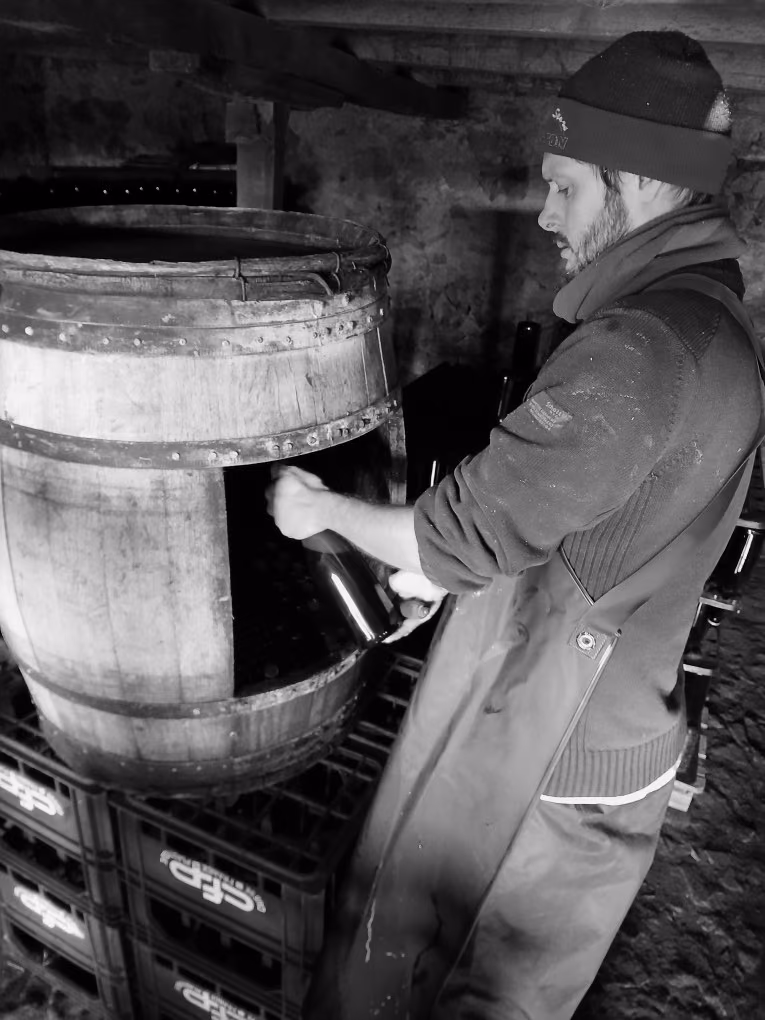 Un producteur devant un tonneau en bois, des caisses de bouteilles au premier plan